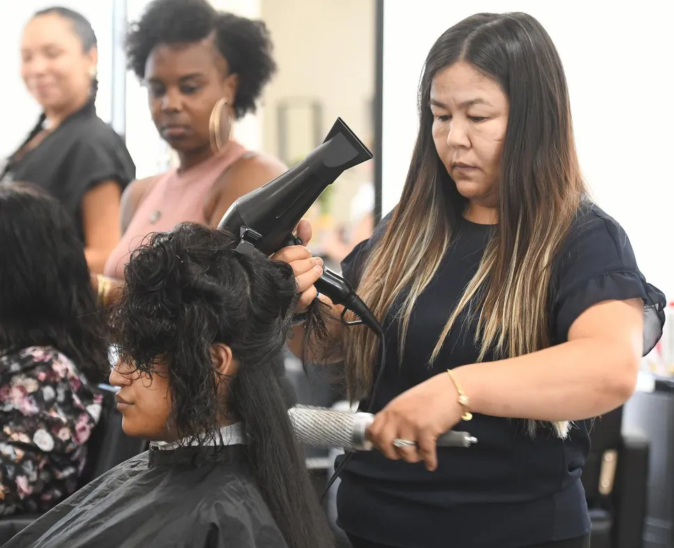 Sima is seen here working on Maha Tariq's hair. Instructor Aisha Simpson is in the background.