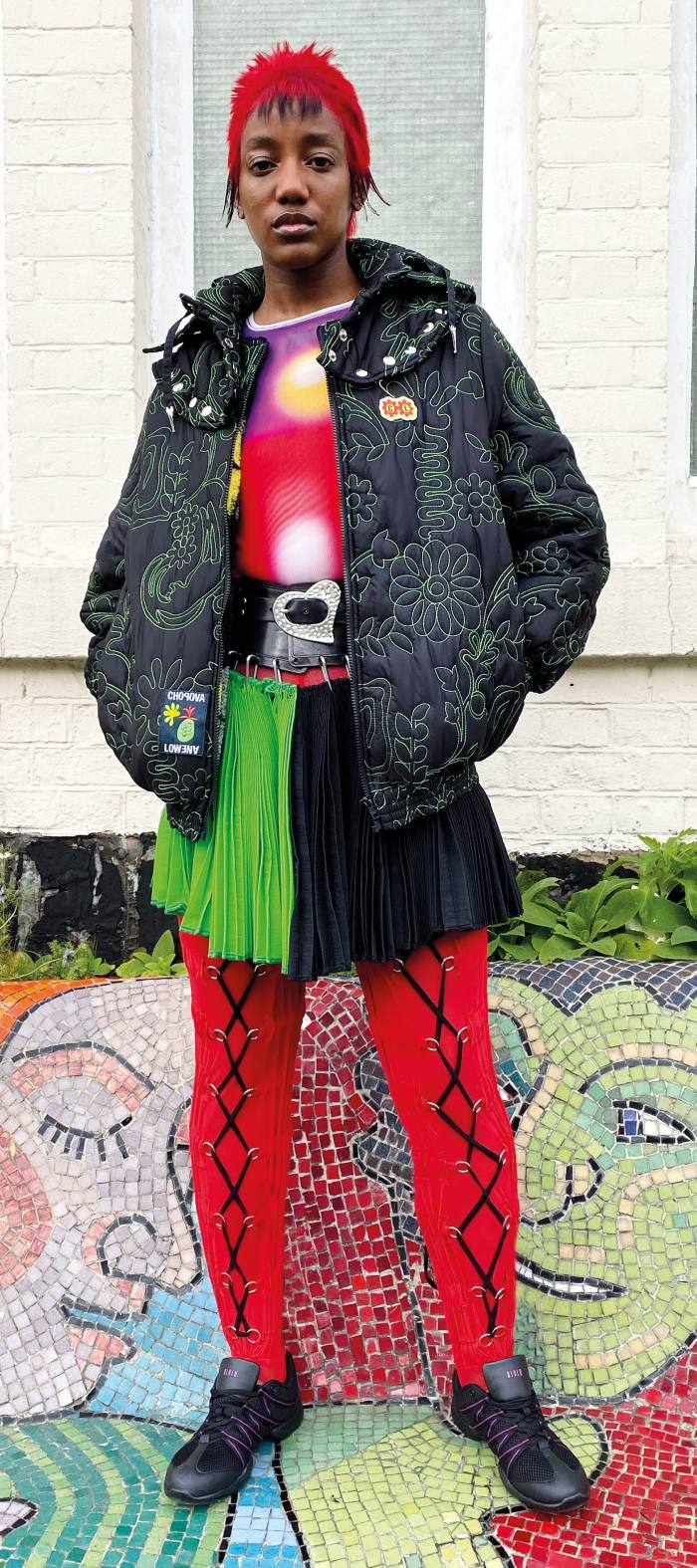 A model wears a dark jacket and black-and-green skirt over a red top and red tights