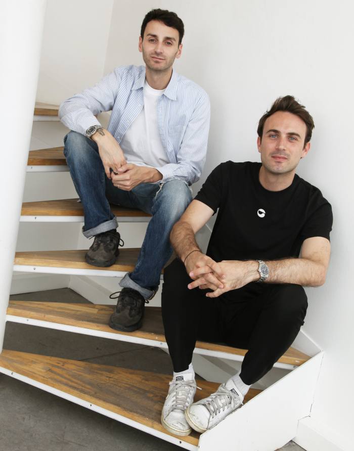 Sébastien Meyer and Arnaud Vaillant, wearing casual clothes, sit on the steps of a staircase